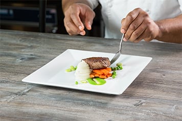 A chef arranges a blend of lima beans and peas onto a plate using a spoon