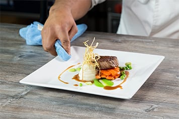 A chef wiping a plate clean