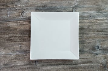 a white, square plate on a wood table