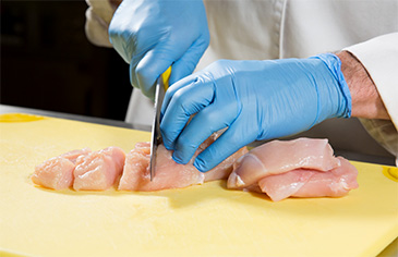 cutting raw chicken into cubes