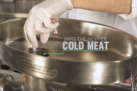chef's gloved hand inserting cold meat into the hopper of a meat grinder