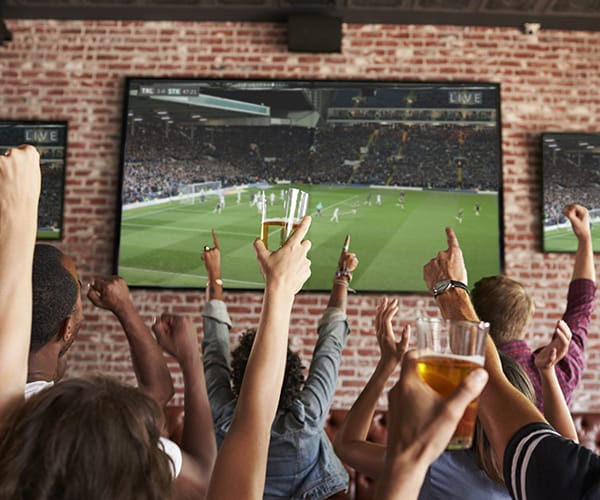 People raising glasses and hands in front of football game on screen