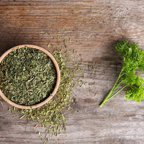 Dried oregano in a bowl next to fresh parsley