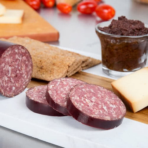 sliced Lebanon bologna on a plate with crackers and dip