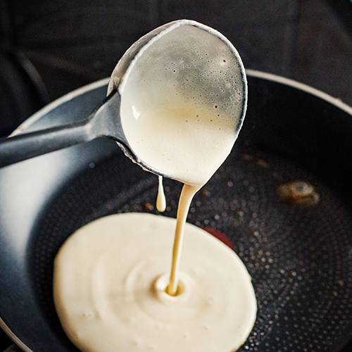 ladling pancake batter into a pan