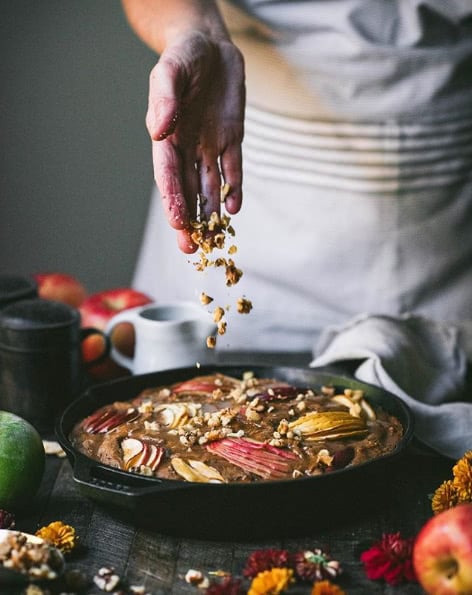 Hand tossing walnuts on an apple walnut cake in a cast iron pan