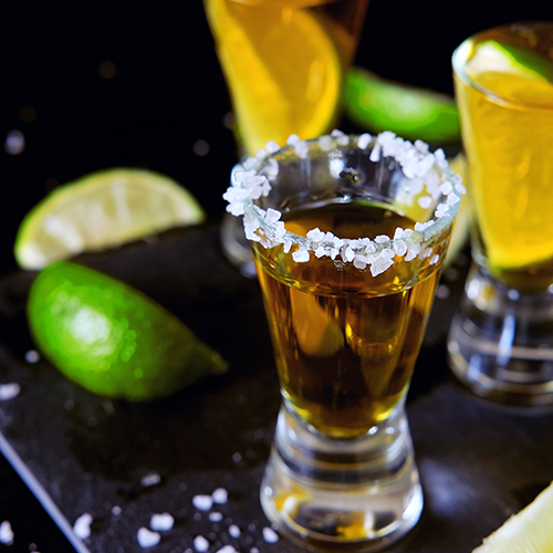Shot glass of tequila with salted rim and lime garnishes