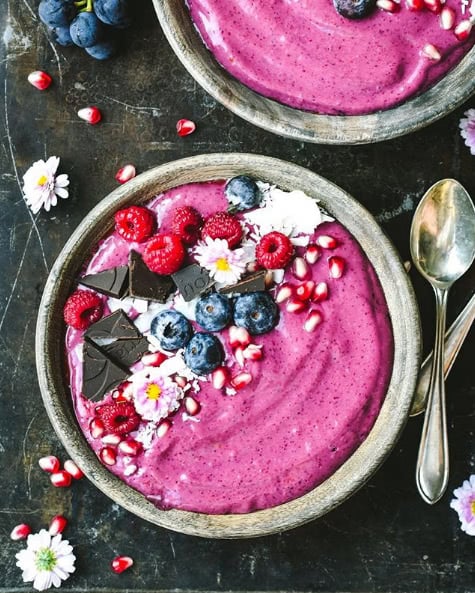 Pink smoothie bowl with berries on top and spoon next to bowl