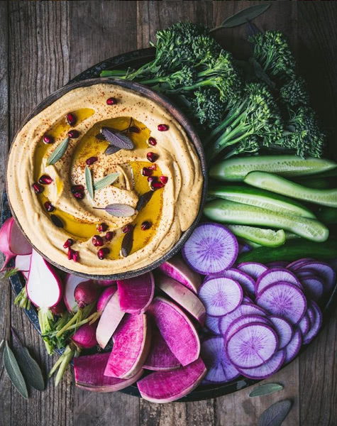 Plate of hummus with a colorful vegetable assortment on a wood table