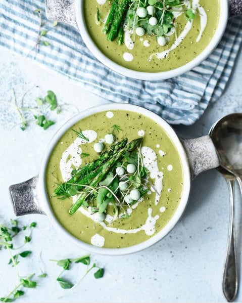 White bowls of pea soups with herb garnishes