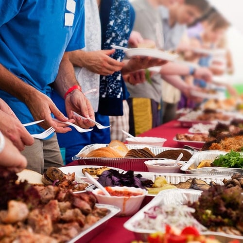 People taking food from a buffet on a picnic table