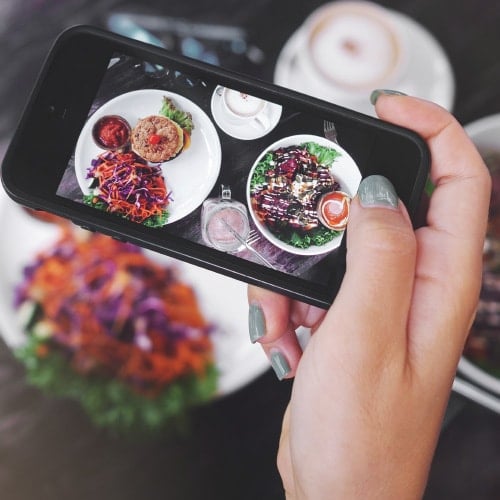 closeup of an iphone taking pictures of a colorful plate of food