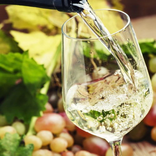 pouring white wine into glass with elegant food behind it for a solo diner