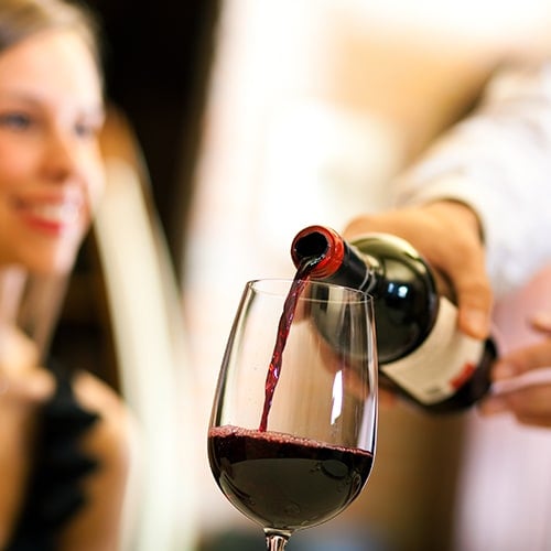 Server's hands pouring wine in front of female guest