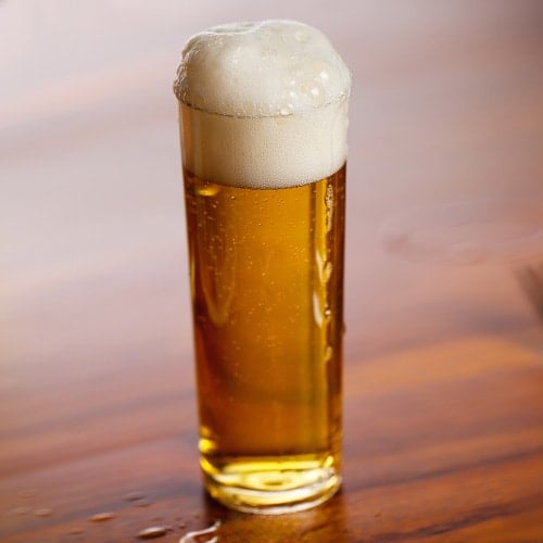 Small straight-sided glass filled with light-colored beer with a frothy head