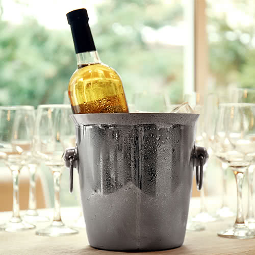 chilled wine bucket with full white wine bottle inside and wine glasses behind bucket