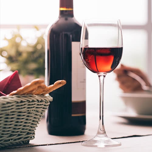 glass of red wine and red wine bottle with basket of breadsticks at a BYOB restaurant