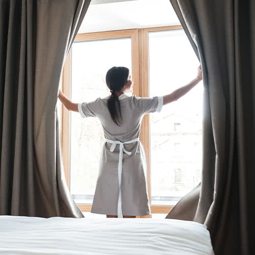 hotel housekeeper opening drapes and letting the sun shine into hotel room
