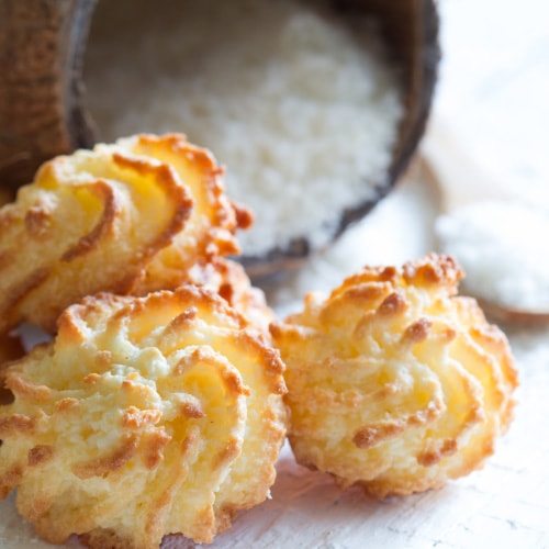 three golden macaroons with a bowl and spoonful of shredded coconut