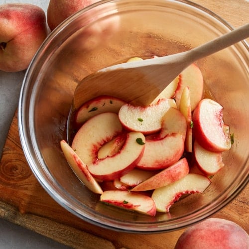 a bowl of sliced peaches with a wooden spoon