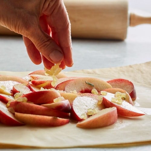 a hand adding candied ginger to an unbaked peach galette