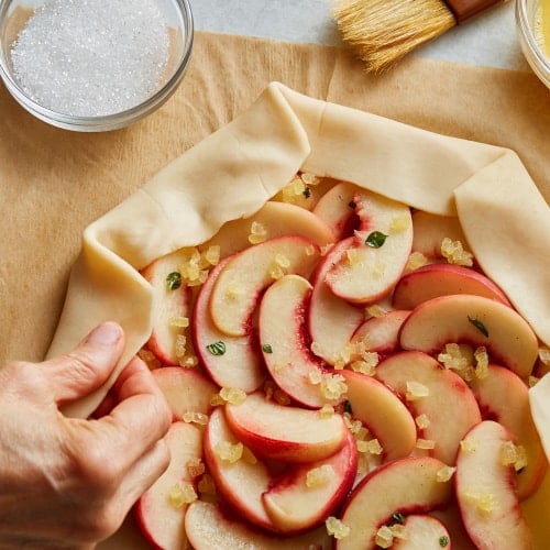 A hand folding the dough on an unbaked peach galette
