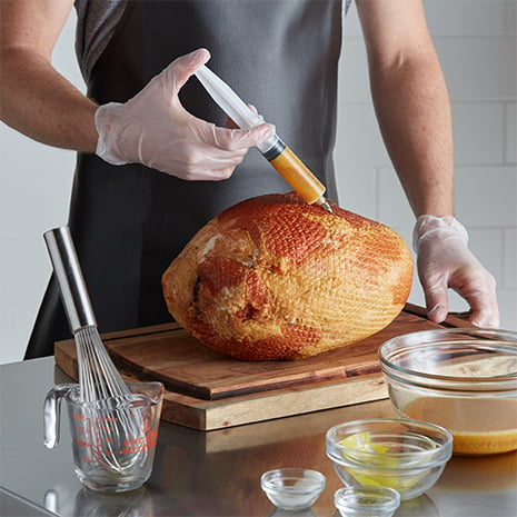 A chef injecting a ham with marinade