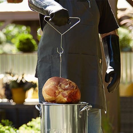 A chef lowering the ham into an outdoor fryer
