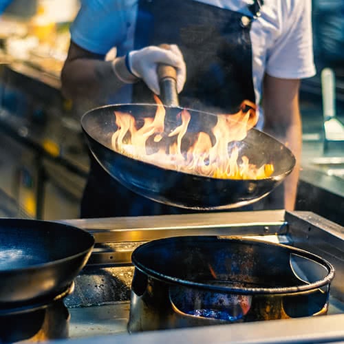 El cocinero sosteniendo un wok sobre un quemador de wok