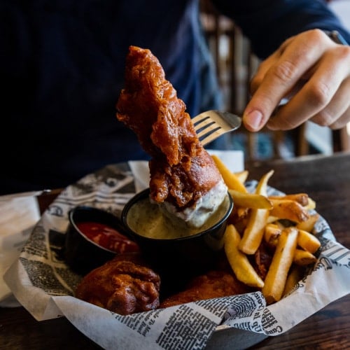 hand lifting up a piece of barbecue chicken on a fork atop a platter of chicken and fries