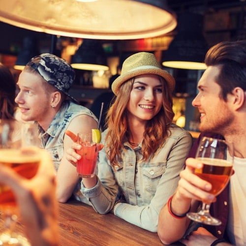 one man looking away, and a woman and man looking at each other while holding drinks at bar
