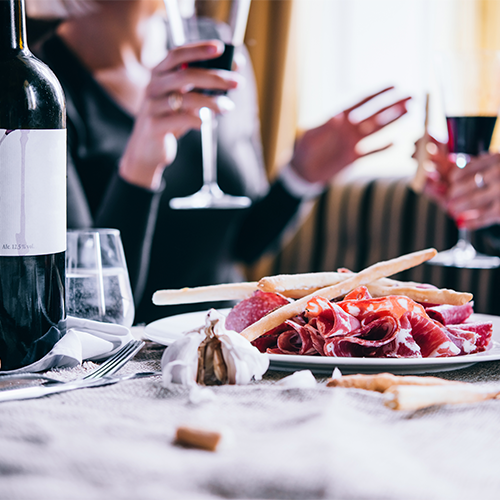 charcuterie board on table with woman and other person holding red wine glasses out of focus