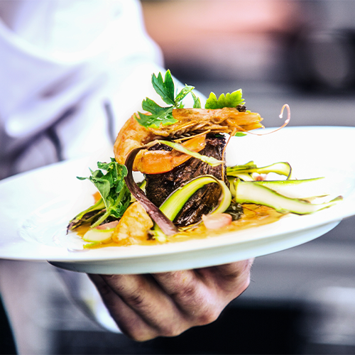 chef holding white plate with steak, shrimp, and assorted colorful vegetables