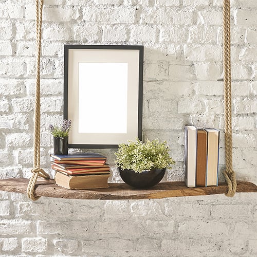 books and flower pot on hanging shelf with white brick behind it