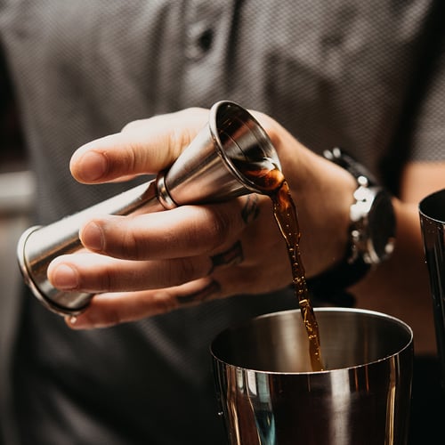 a bartender using a jigger to measure and pour drinks