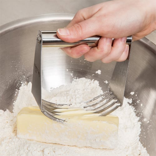 one hand using a pastry blender to add shortening to a bowl of flour