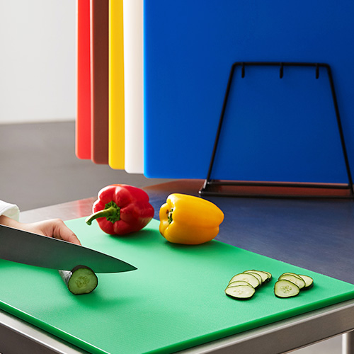 Knife cutting through cucumber on green cutting board with color coded cutting boards behind it