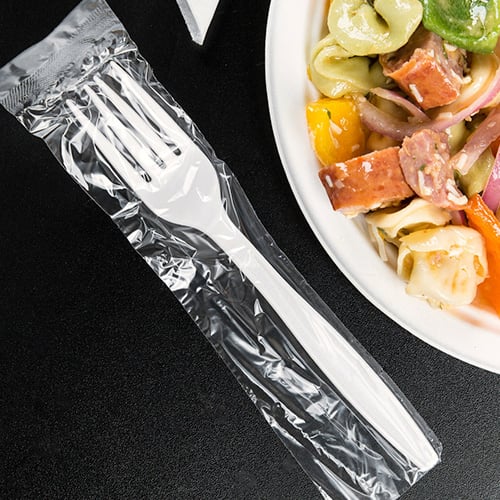 Individually wrapped plastic fork next to corner of plate of food