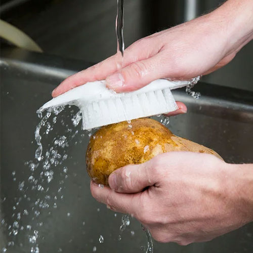 Cleaning a potato with a vegetable prep brush