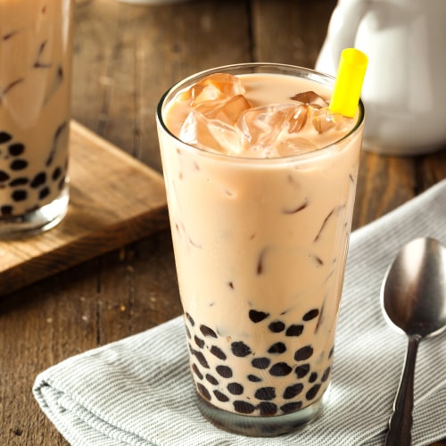 Bubble tea with boba balls and ice on top of napkin next to spoon