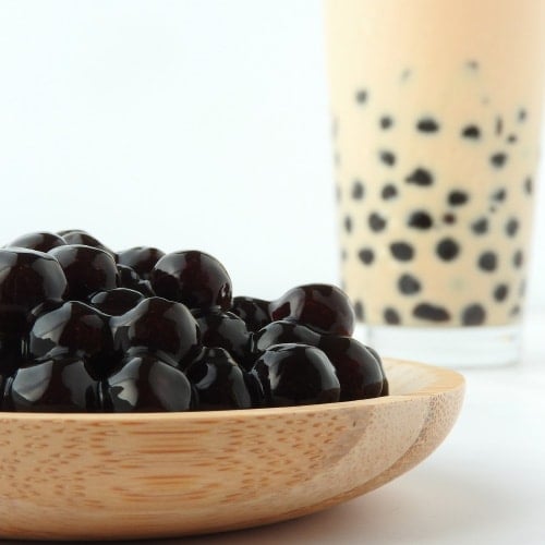 Bowl of boba balls with glass of bubble tea in the background