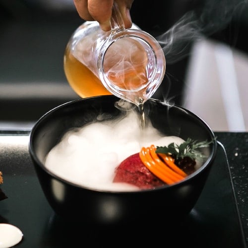 chef pouring liquid into smoking molecular gastronomy pan