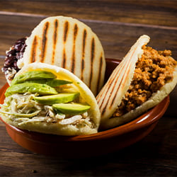 three arepa cornmeal cakes sliced open and filled with toppings