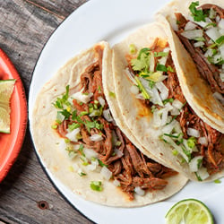 three soft shell tacos filled with shredded meat, diced onions, and cilantro