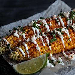 two ears of grilled corn topped with spices, herbs, and crema