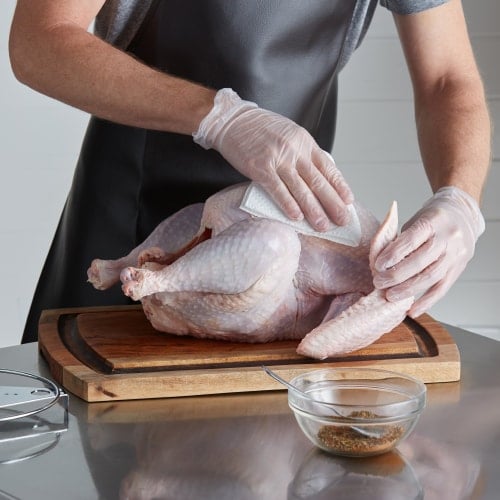 hands patting down turkey on cutting board to become dry before deep frying turkey