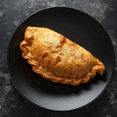 Traditional Cornish pasty filled with beef meat, potato and vegetables on black plate
