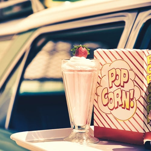 Food tray in window of car with milkshake and popcorn