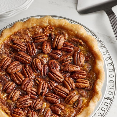 Pecan pie in glass pie dish with silver pie server sitting beside on table