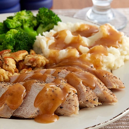 Turkey dinner on plate with sliced turkey, mashed potatoes, broccoli and gravy.